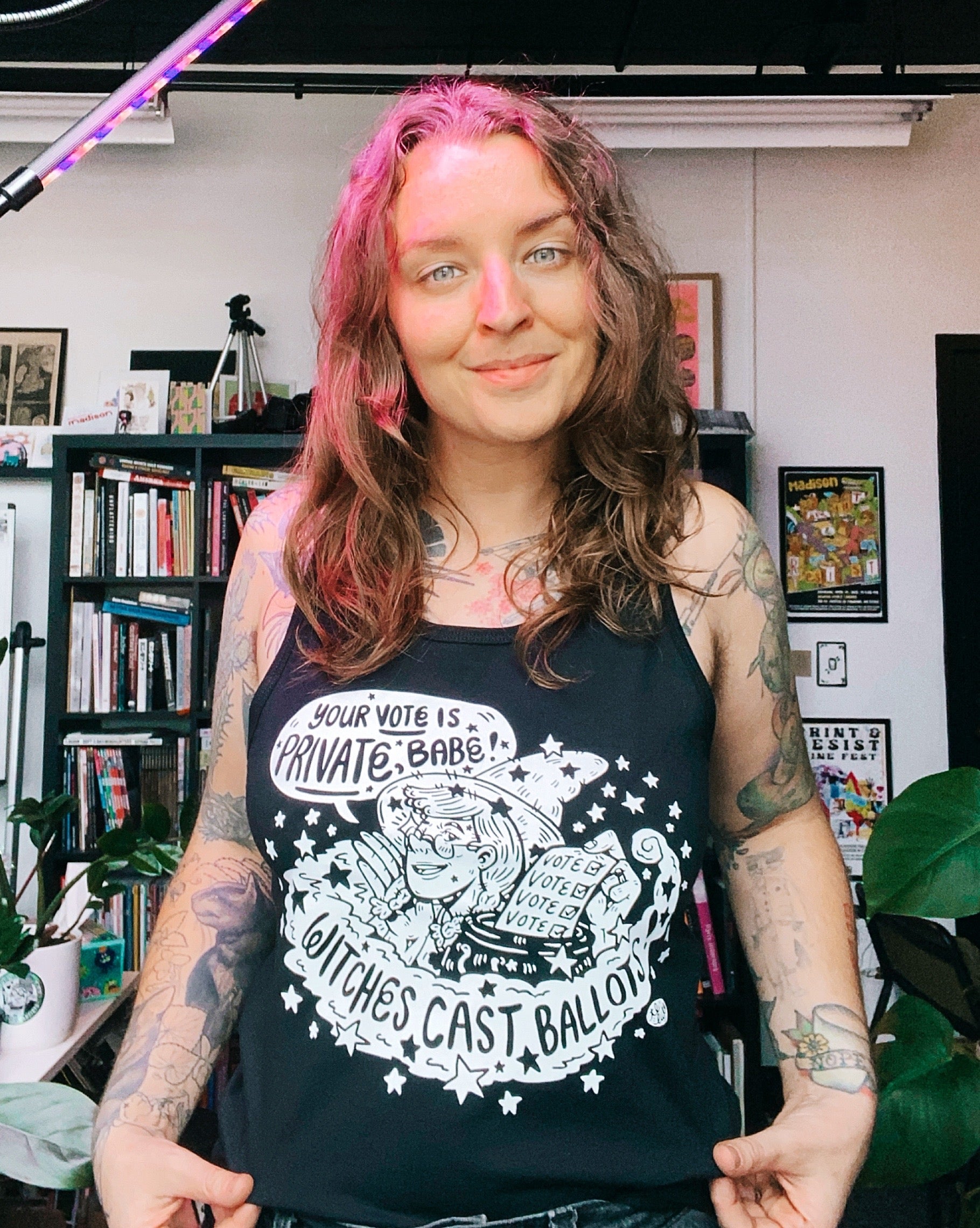 A person wearing a black tank top with a graphic print that includes the phrase 'YOUR VOTE IS PRIVATE BABY!' and various political-themed illustrations.